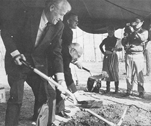 Vintage black & white photo of three men putting shovels into the ground for a ceremonial groundbreaking.